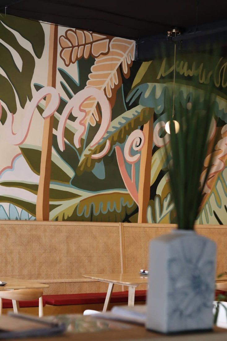 halina dining room mural HALINÁ Modern Filipino Kitchen + Bar Hand-painted tropical leaf mural above a rattan banquette in the Halina dining room
